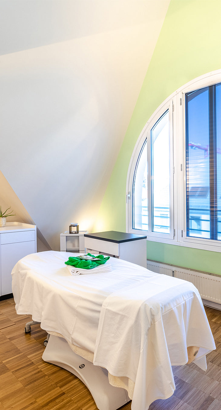 Behandlungsraum in Mayr's DaySpa Pasing mit einer Liege vor einem großzügigen Fenstern bei entspannender Atmosphäre